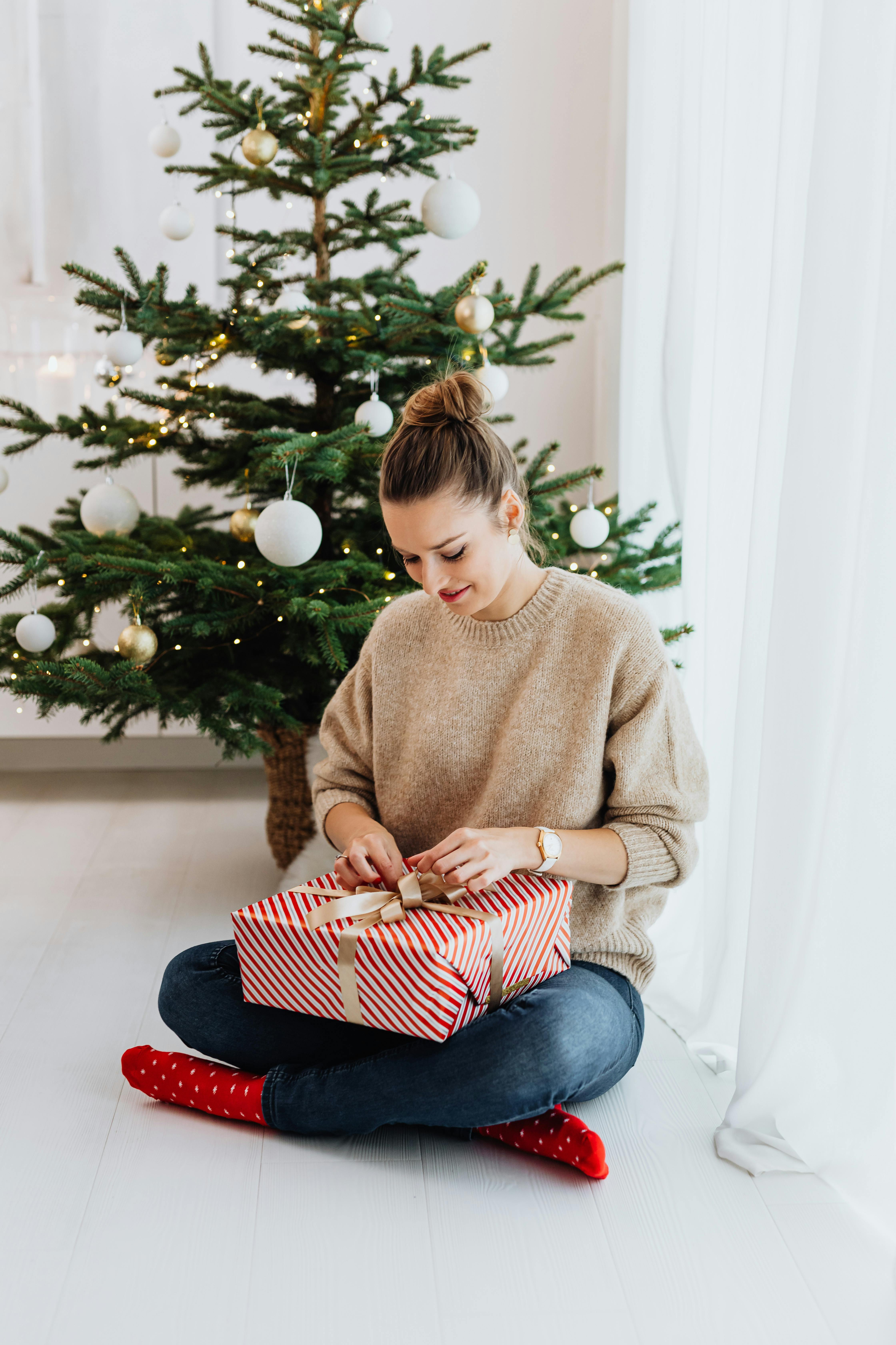 a woman sitting near the christmas tree opening a gift box