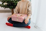 一名成年妇女坐在室内装饰好的圣诞树旁，手里拿着包装好的礼物