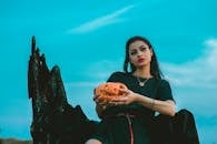 一位黑发时尚的哥特风女子在蓝天下捧着一个雕刻的南瓜