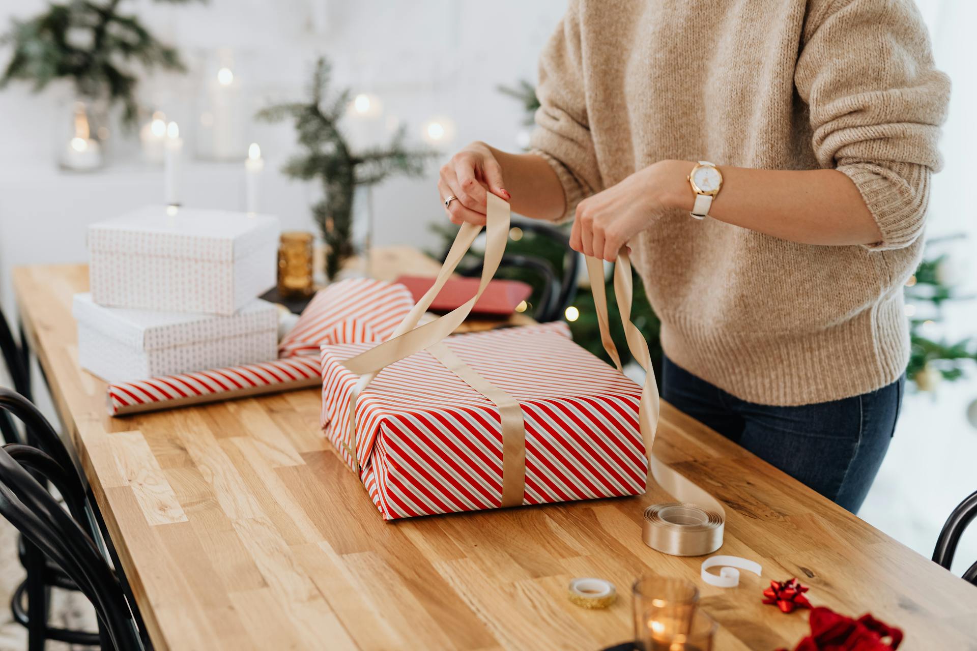 Woman wrapping Christmas gifts with ribbon. Cozy indoor holiday setting.