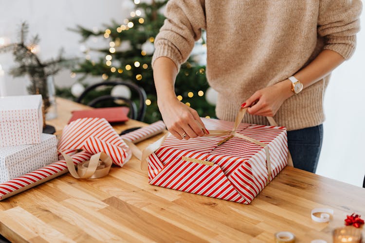 Woman Wrapping Gift Near Christmas Tree