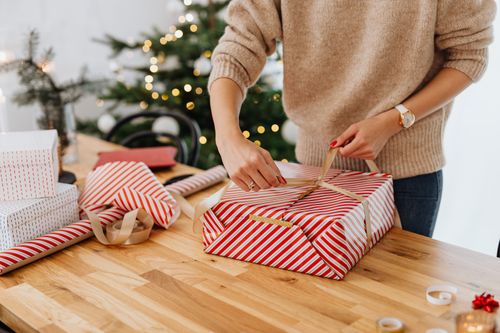 Free A woman wrapping gifts by a Christmas tree, spreading holiday cheer. Stock Photo
