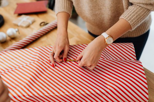 Free Close-up of a woman wrapping a Christmas gift with red striped paper indoors. Stock Photo