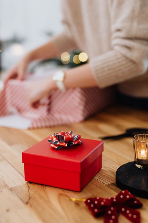 Free A cozy scene featuring a red gift box with a bow on a wooden table during Christmas. Stock Photo
