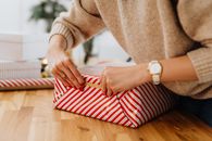 一名妇女在室内用红色条纹包装纸和金丝带包装礼物