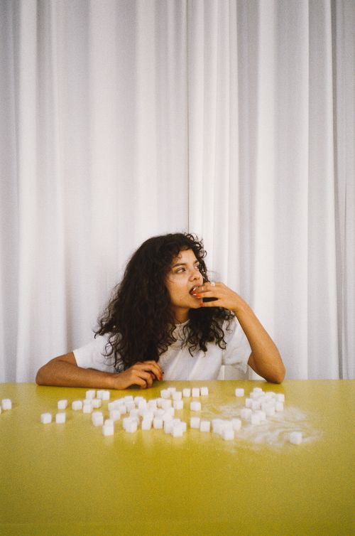 Free A woman at a yellow table with sugar cubes, symbolizing diet choices. Stock Photo