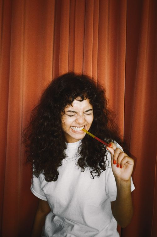 Free A cheerful woman enjoying a gummy candy in front of a red curtain backdrop. Stock Photo