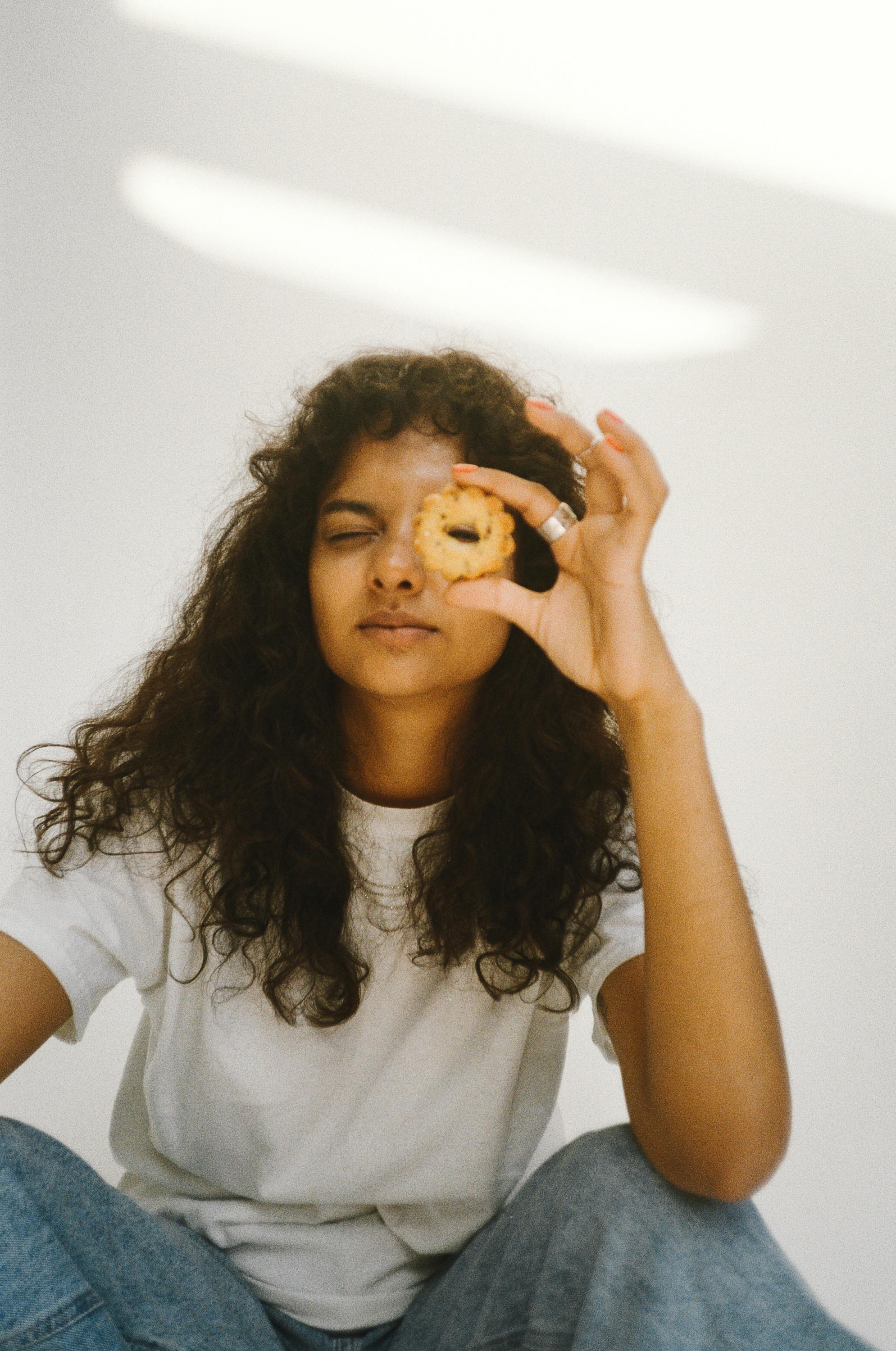 Portrait of a young woman playfully posing with a cookie indoors.