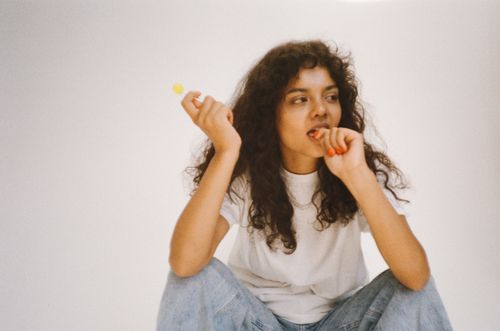 Free Fashionable woman with curly hair posing with a lollipop in a relaxed setting. Stock Photo