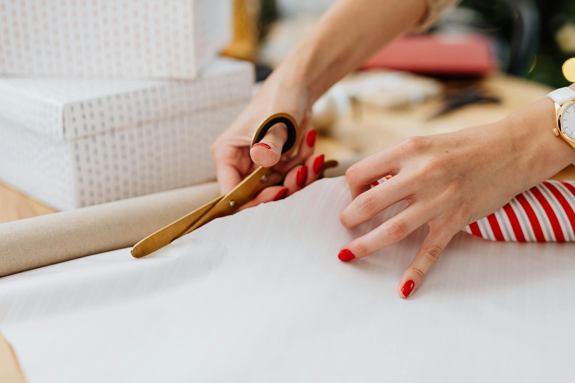 Close-up of hands cutting gift wrap paper with scissors during holiday gift preparation indoors.