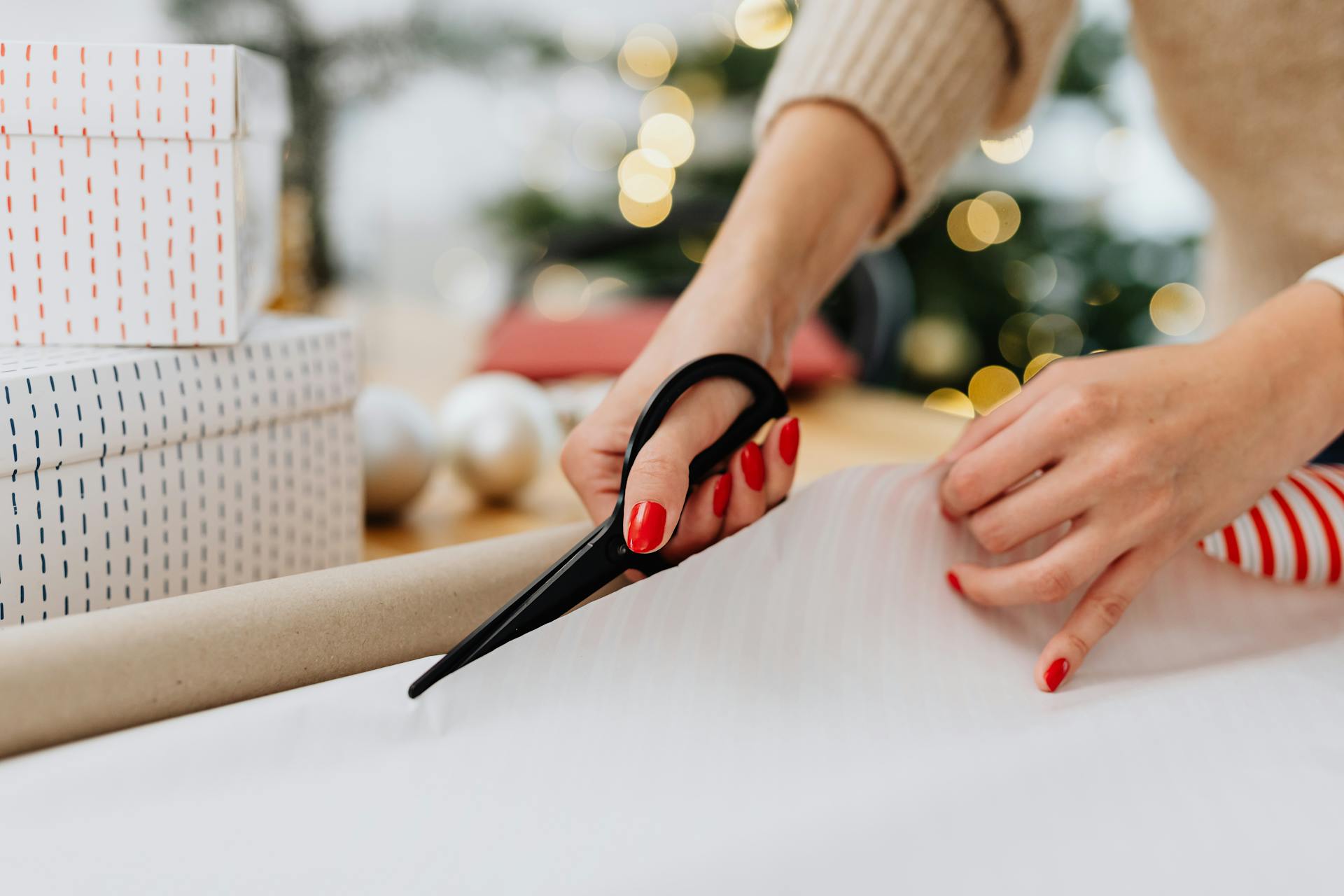 Close-up of a woman cutting wrapping paper, preparing Christmas gifts indoors.