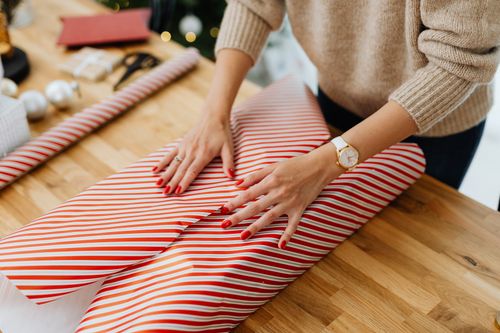 Free A woman wraps a Christmas gift with striped paper on a wooden table indoors, festive and cozy vibe. Stock Photo