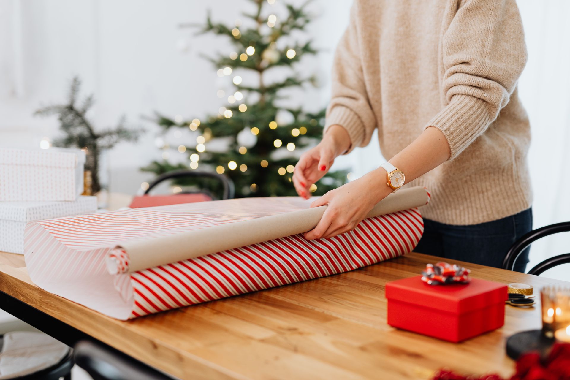 Person wrapping gifts near a Christmas tree, representing holiday joy.