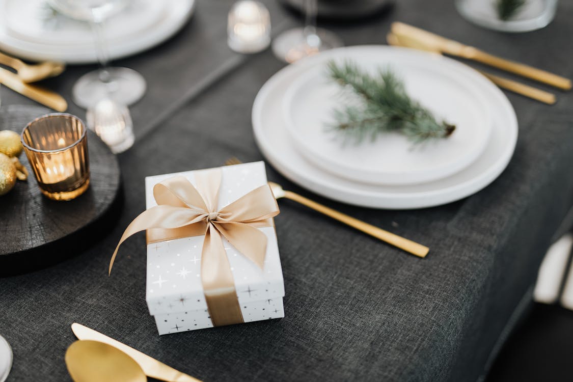 Elegant white and gold gift box on a festive dining table with gold cutlery and candlelight.