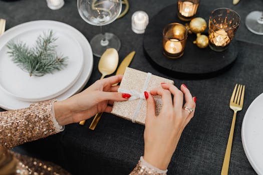 Close-up of hands opening a glittery gift box during a festive holiday dinner setting with candles.