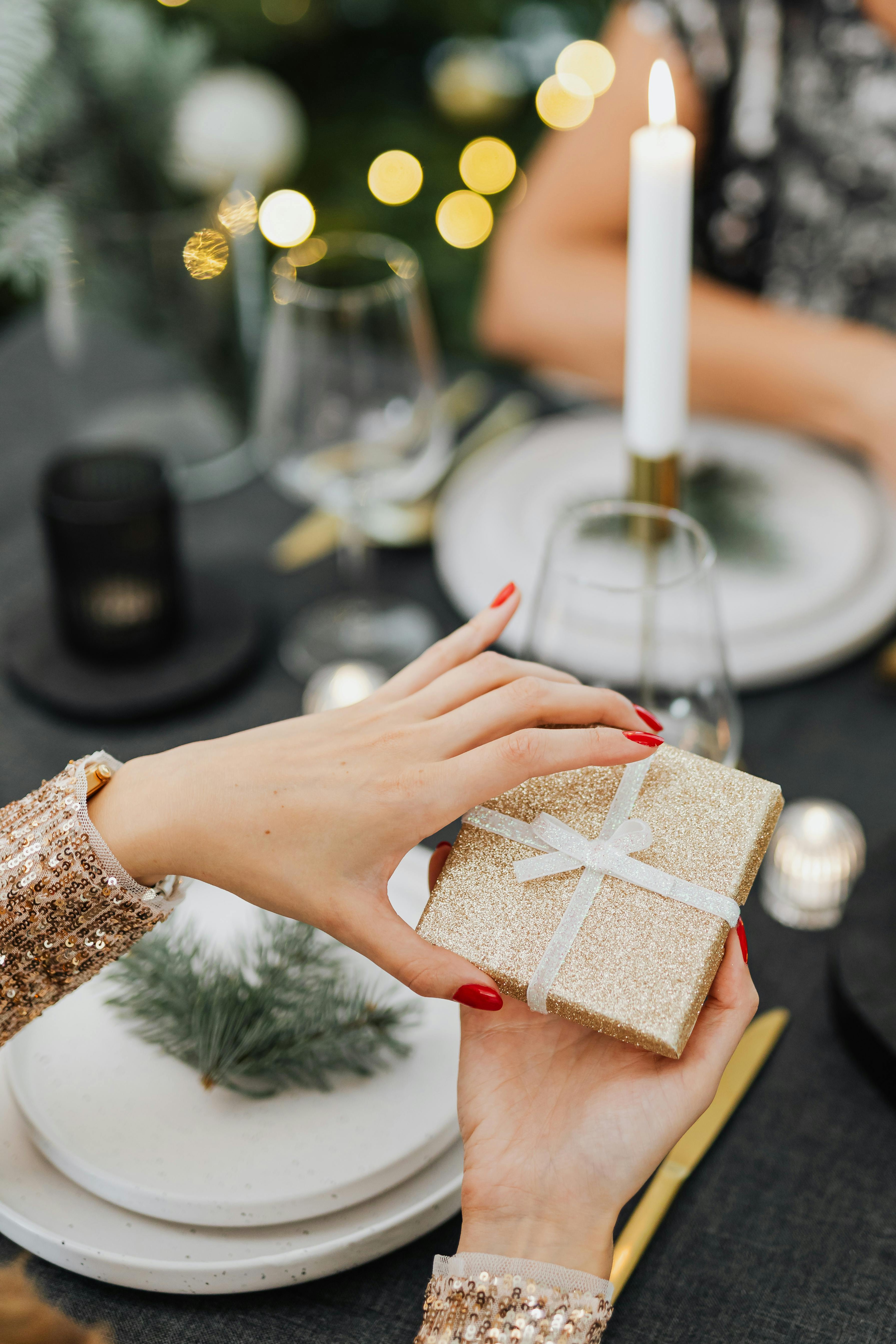 烛光餐桌上，两名女子交换闪闪发光的圣诞礼物的特写镜头