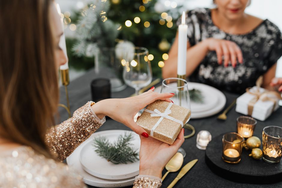 engraved gift ideas for best friends - Women exchanging gifts in a festive setting with candles and holiday decor.