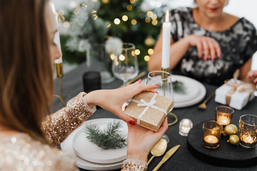 Femme tenant un petit cadeau doré à une table de Noël aux bougies