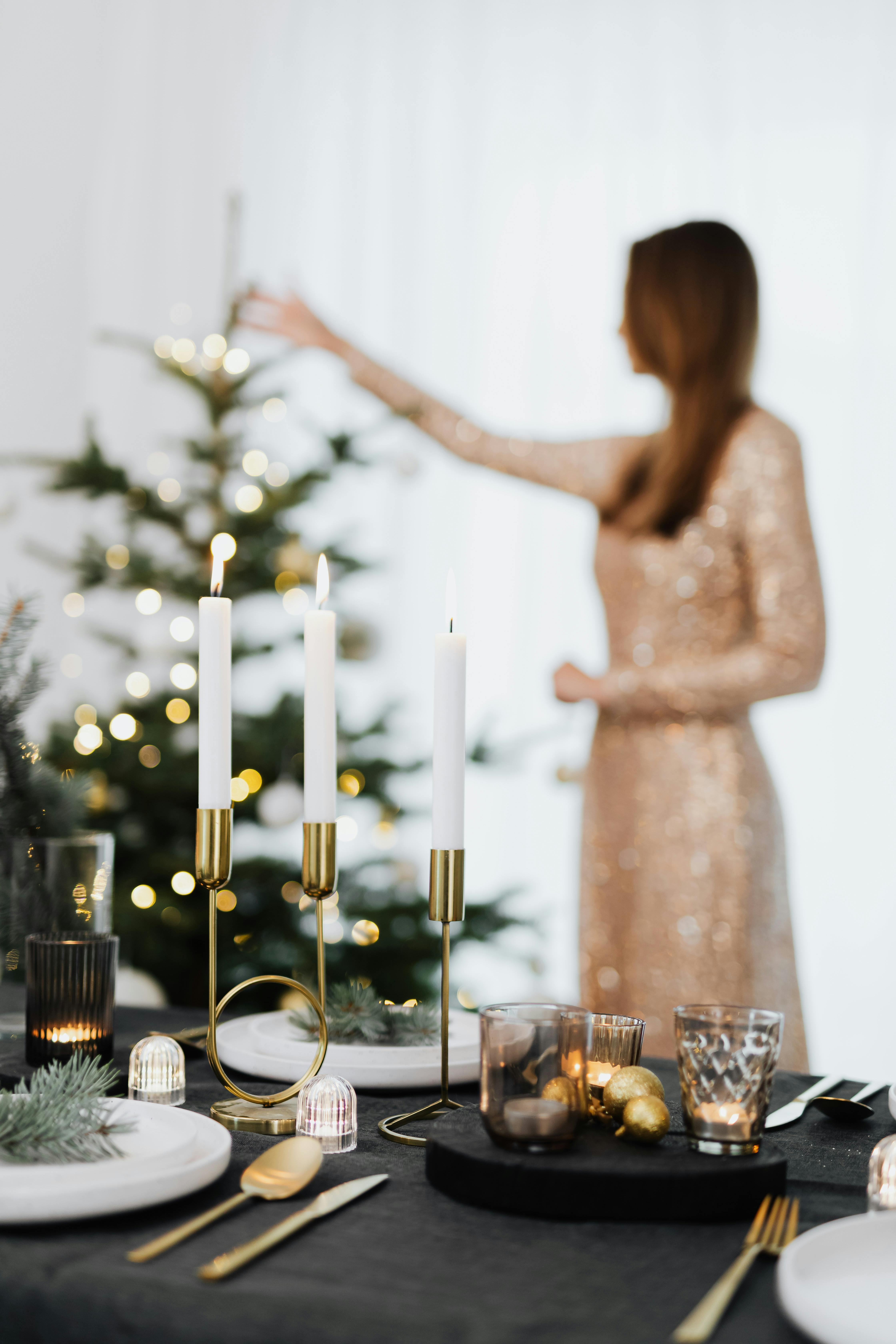 photo of a table setting with a woman standing by the christmas tree in the background