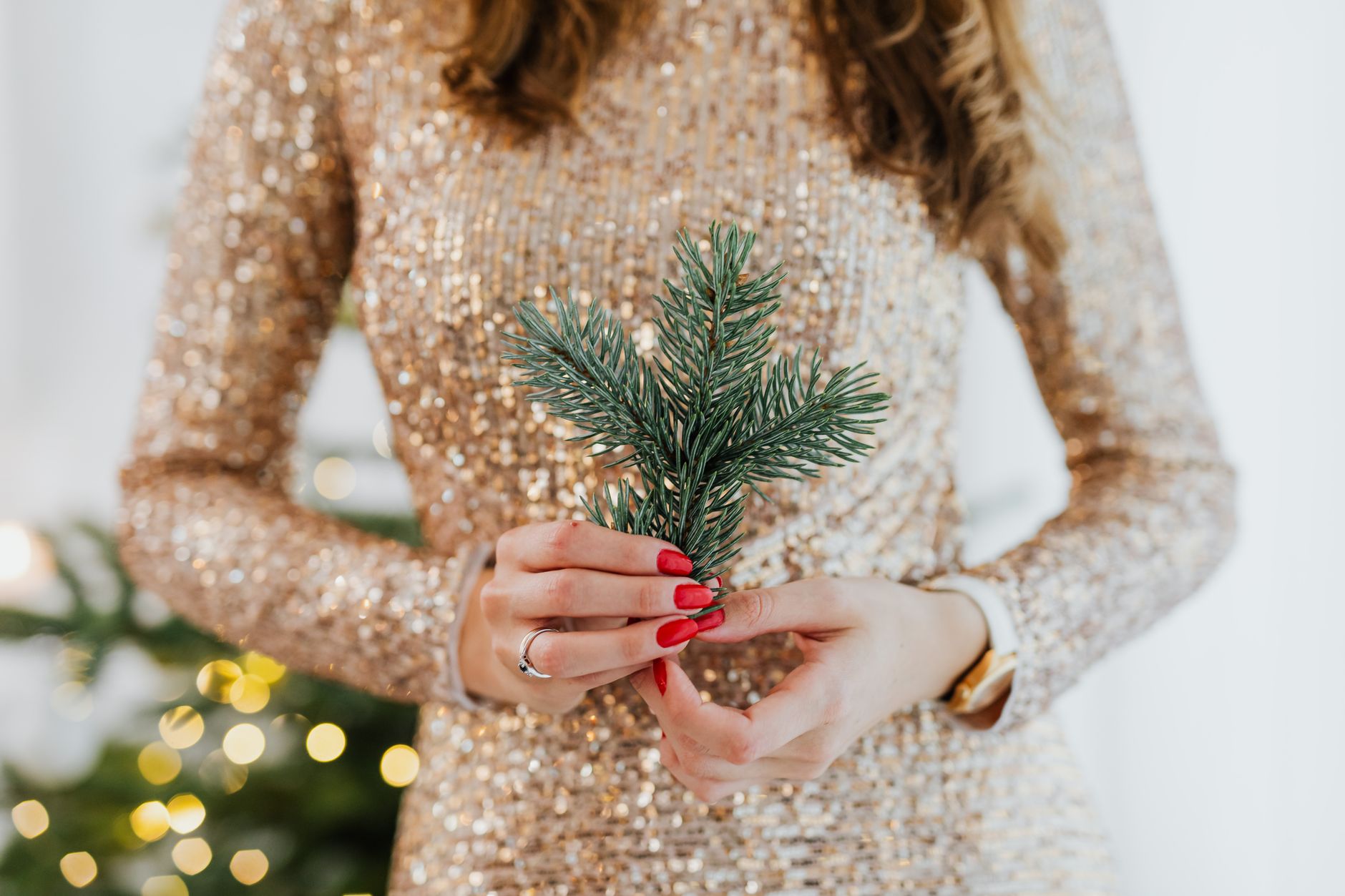 A woman in a sparkling dress holds a spruce twig, embodying holiday elegance and joy.