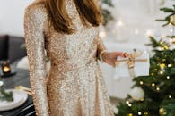 一位身穿闪亮连衣裙的女子在圣诞树旁拿着礼物，充满节日气氛