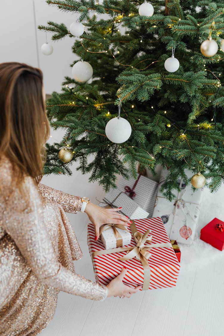 Woman Putting Christmas Gift Under Christmas Tree 