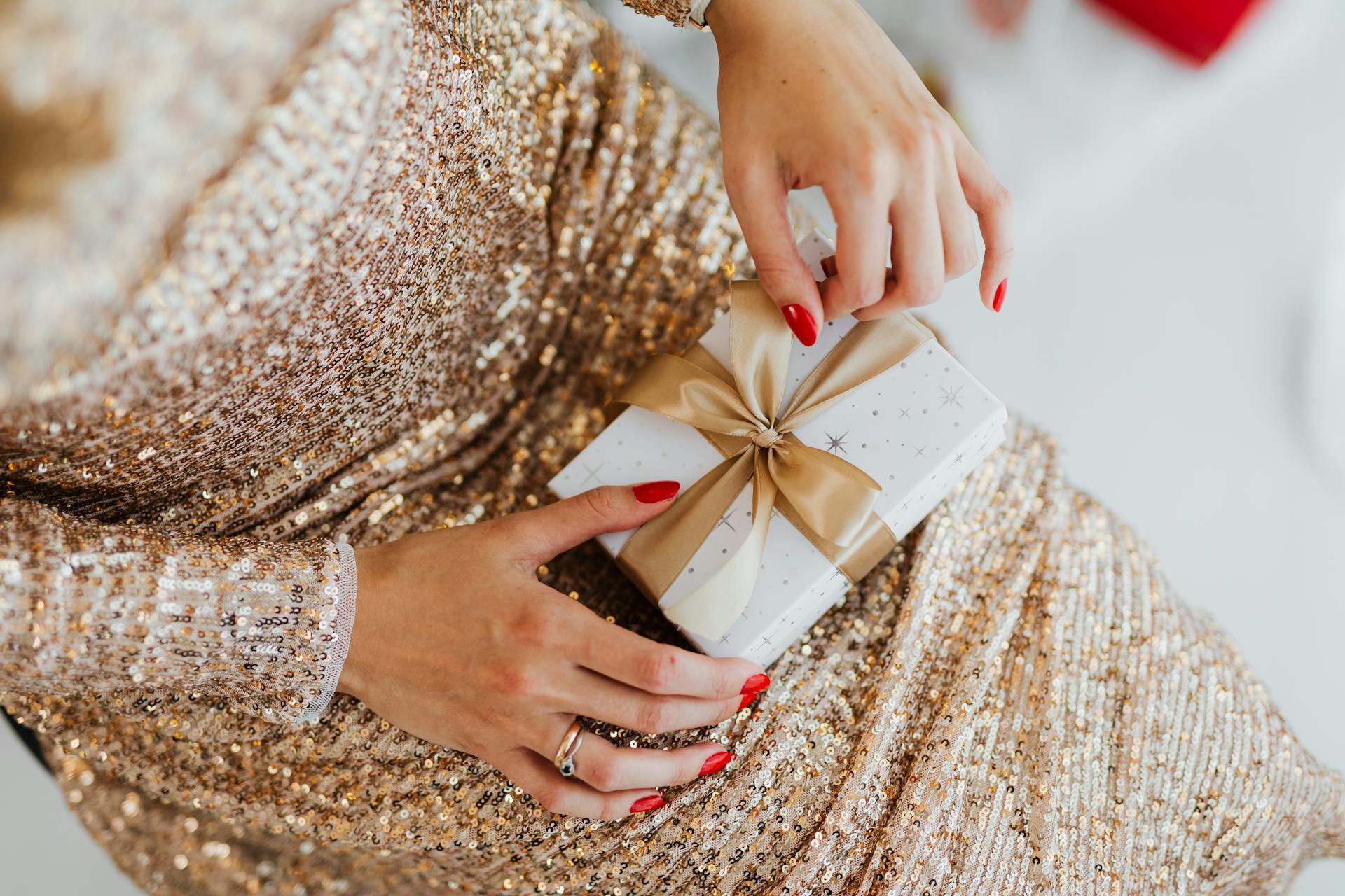 Close-up of woman's hands holding a gift wrapped in shimmering paper and gold ribbon, perfect for festive occasions.