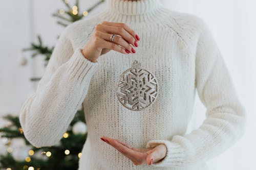 Woman in a White Sweater Holding a Silver Bauble 
