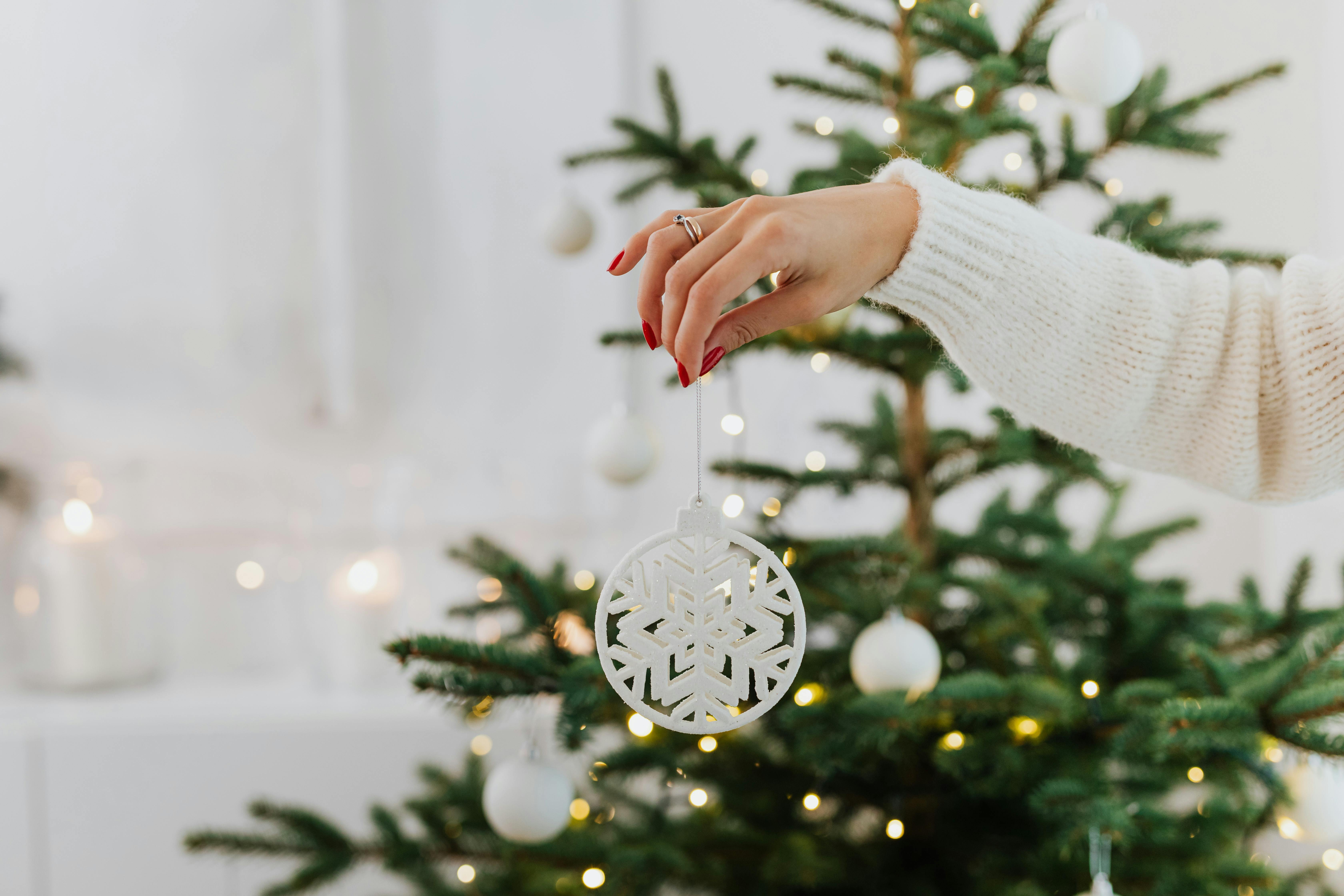 一只手巧妙地将雪花装饰品放在室内装饰好的圣诞树上