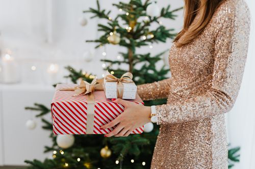 Free Woman in glitter dress holds gifts in front of a decorated Christmas tree. Stock Photo
