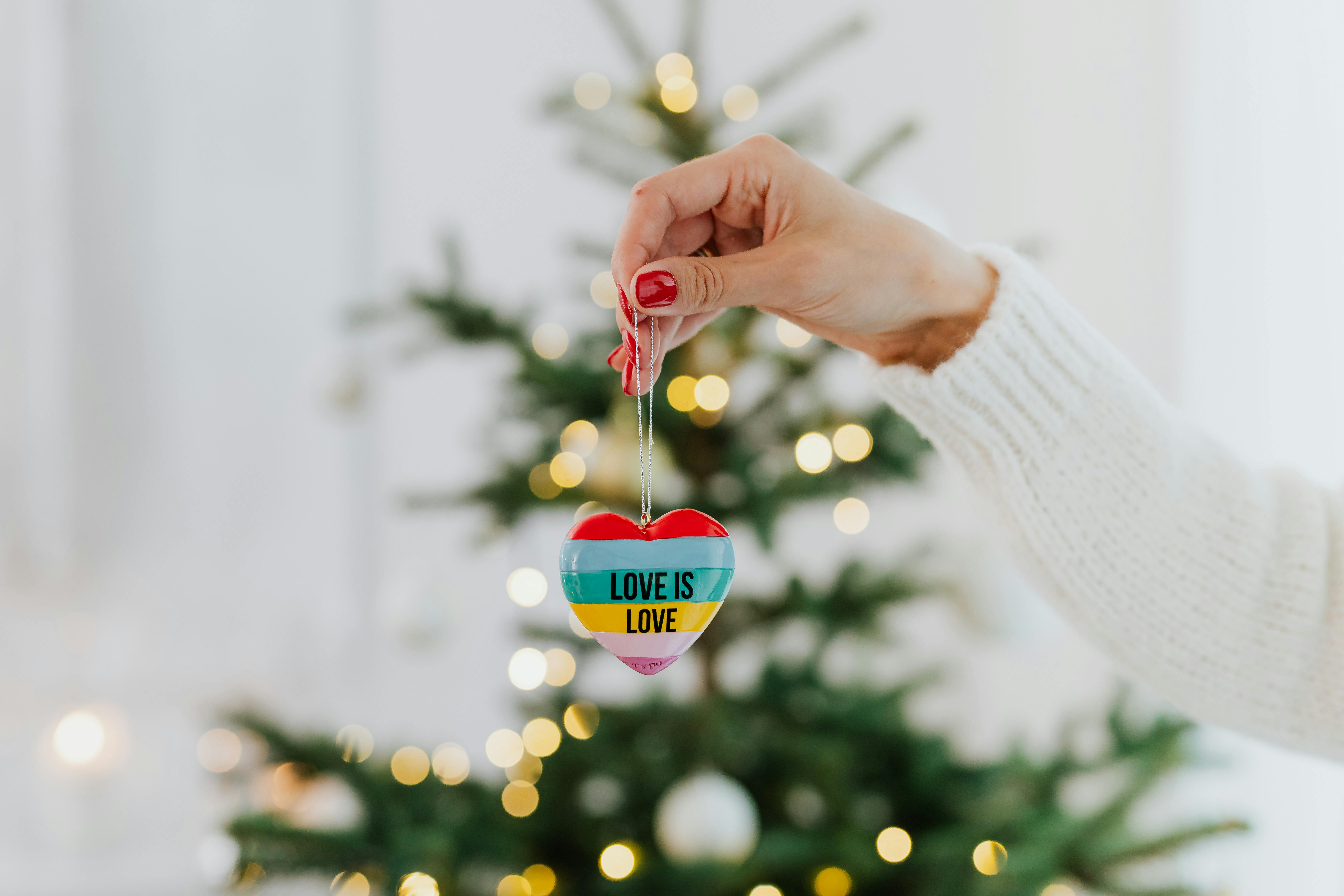 一只手在圣诞树背景下拿着一个写着“爱就是爱”的心形装饰品