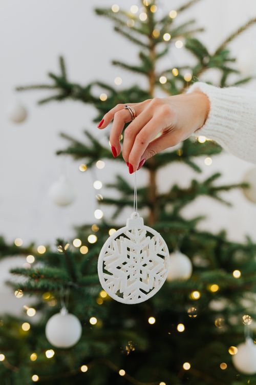 Free A woman's hand hangs an ornament on a Christmas tree branch with festive lights. Stock Photo