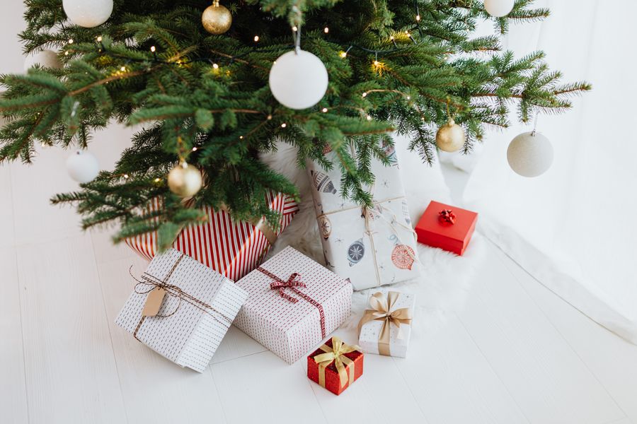 wrapped first Christmas gifts for babies piled under a white and gold Christmas tree
