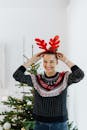 一位戴着驯鹿头带的女人在室内圣诞树旁微笑