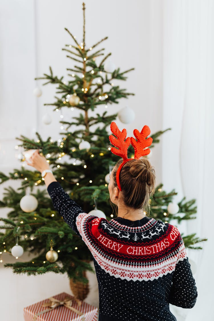 Woman In Red And Black Sweater Putting Ornaments On Christmas Tree