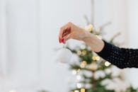 一名妇女在喜庆的室内环境中，手持一个白色圣诞小饰品，身旁有一棵散景效果的圣诞树