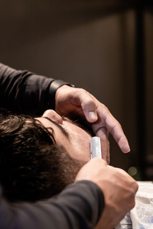 Free A barber skillfully uses a straight razor to shave a client's beard, highlighting precision grooming. Stock Photo