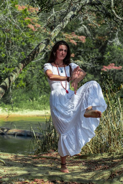 Free Full body of barefoot female in traditional white dress gesticulating while performing ritual dance in forest near lake in summer Stock Photo