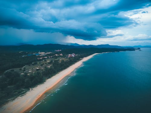 Aerial view of bright blue sea water washing sandy coastline with green trees under cloudy sky