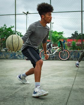 Young male athlete dribbling a basketball outdoors on a court during the day, showcasing skill and motion.