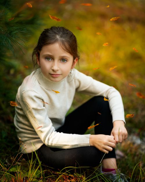 Free High angle of calm cute girl in casual clothes sitting on grassy meadow amidst fallen leaves and looking at camera in autumn park Stock Photo