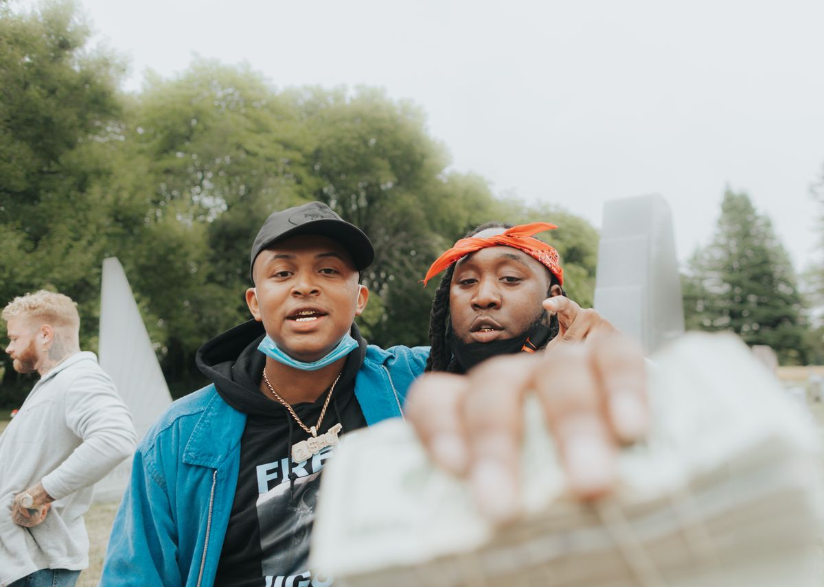 Two friends outdoors holding stacks of cash, exchanging money