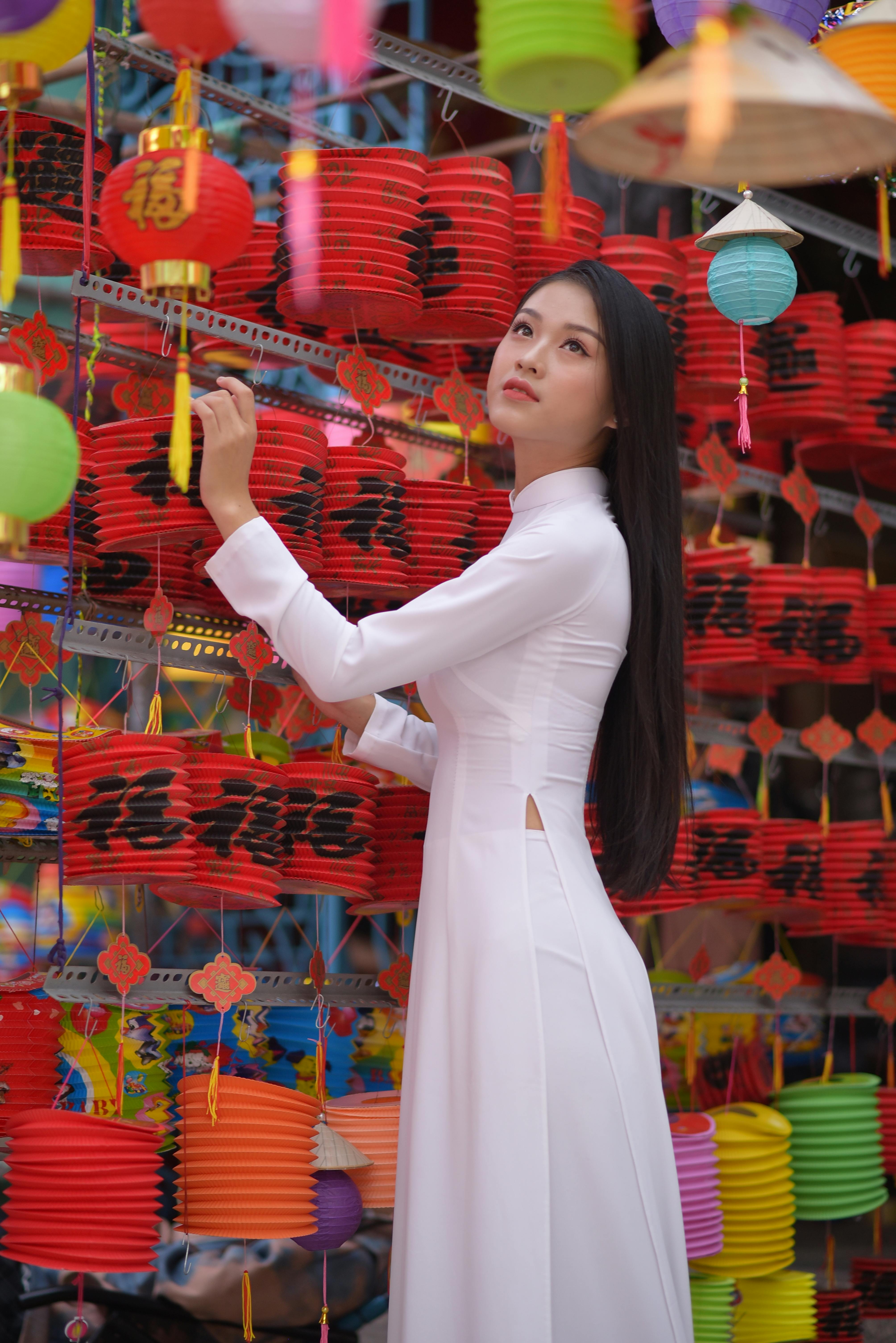Asian woman wearing ao dai surrounded by colorful Chinese lanterns, showcasing cultural beauty.