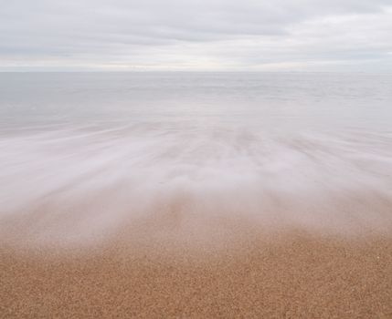 Gentle waves wash over a tranquil beach, creating a peaceful coastal scene.
