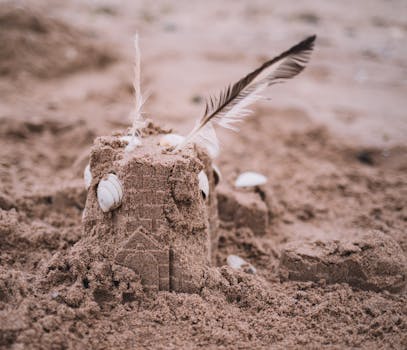 Artistic sand castle adorned with feathers and shells on a beach, capturing a serene coastal vibe.