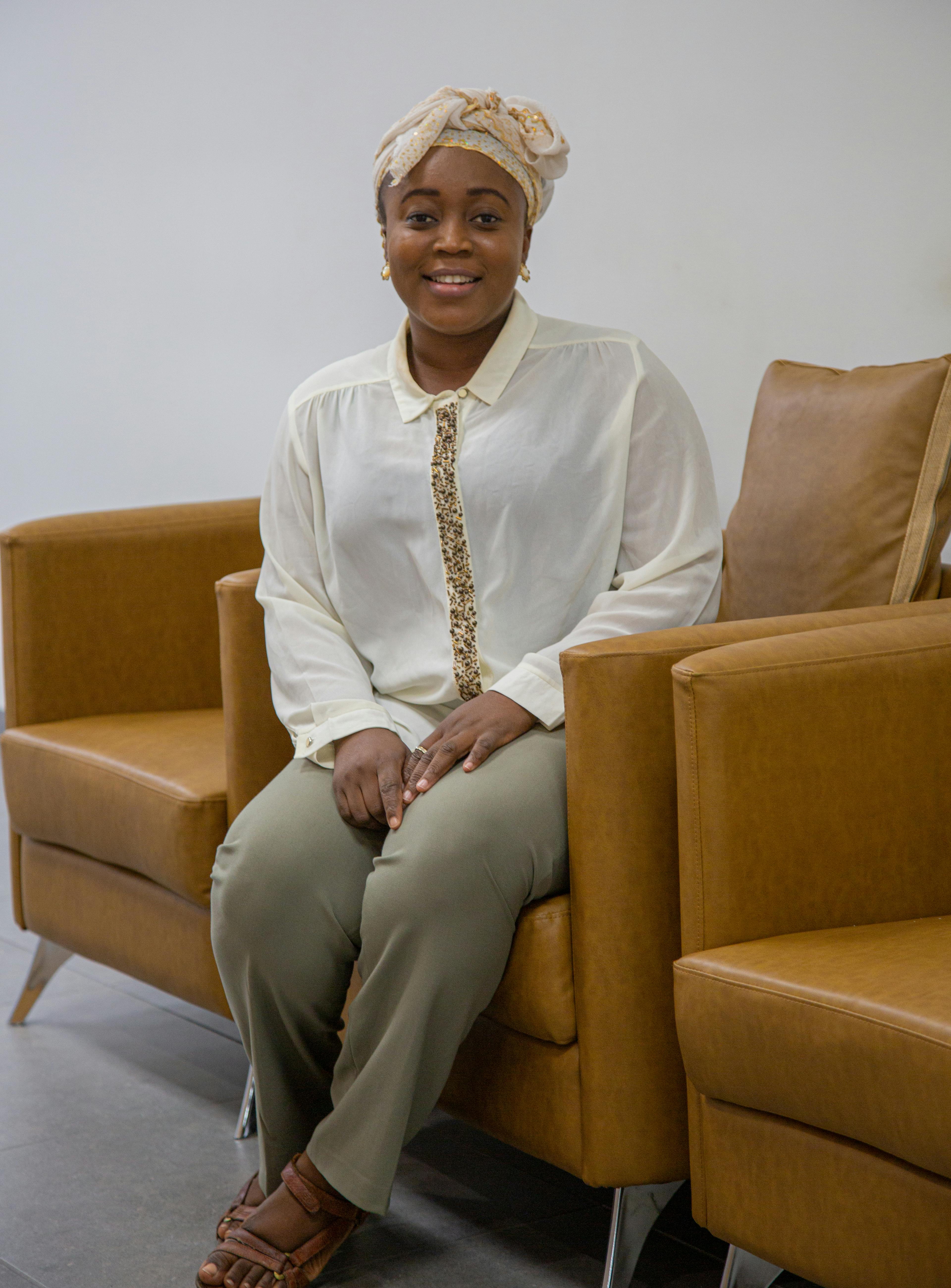Black woman sitting and smiling on a sofa in a modern living room, wearing relaxed attire.