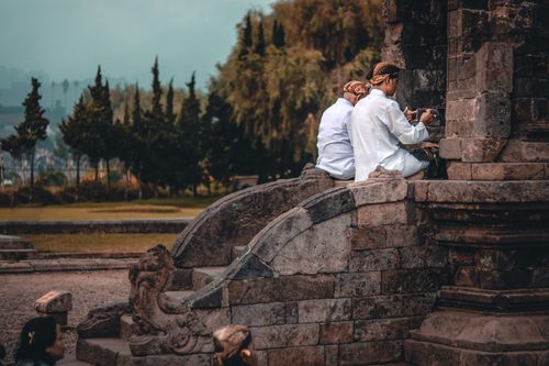 Free Back view of anonymous ethnic male in white wear praying on staircase of old church near trees Stock Photo
