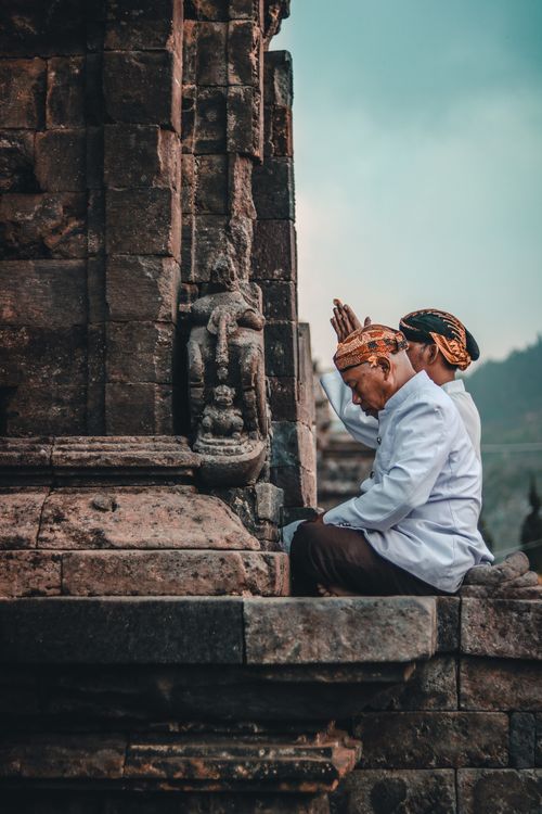 Free Side view of unrecognizable ethnic Buddhist male in traditional clothes praying with closed eyes near aged church Stock Photo