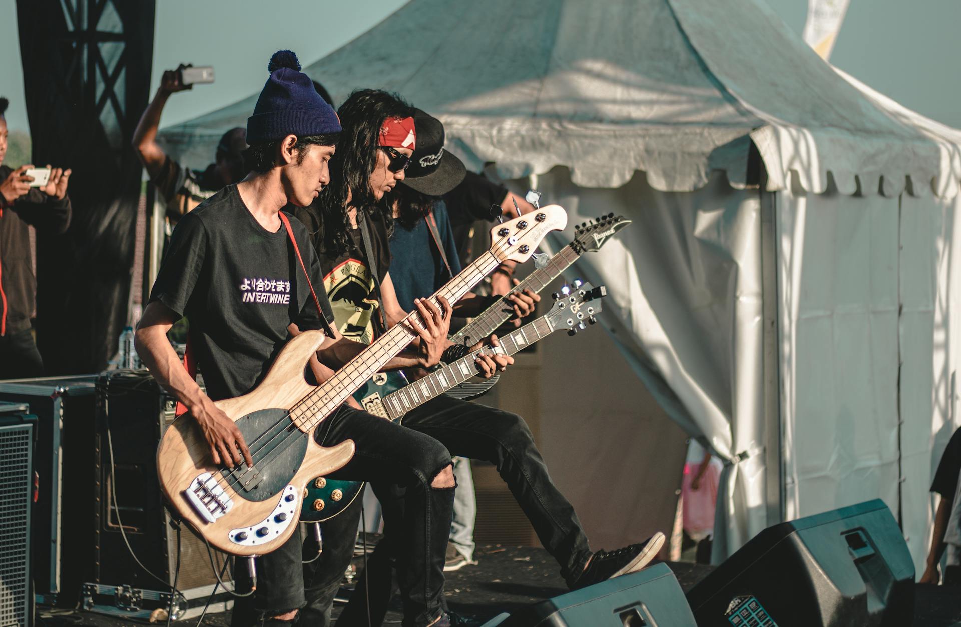 Live outdoor concert featuring a rock band with electric guitars and enthusiastic men performing on stage.