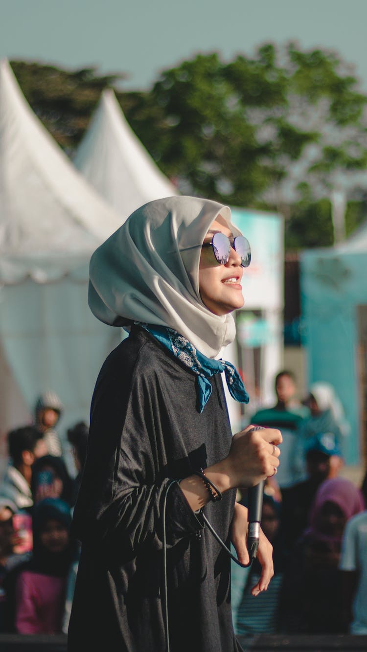 Positive Muslim Woman With Wired Microphone Standing Near Tent